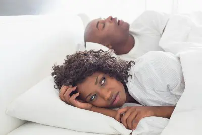 annoyed woman laying next to her snoring husband in bed