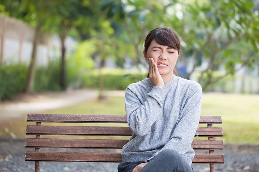 woman with jaw pain sits on a park bench