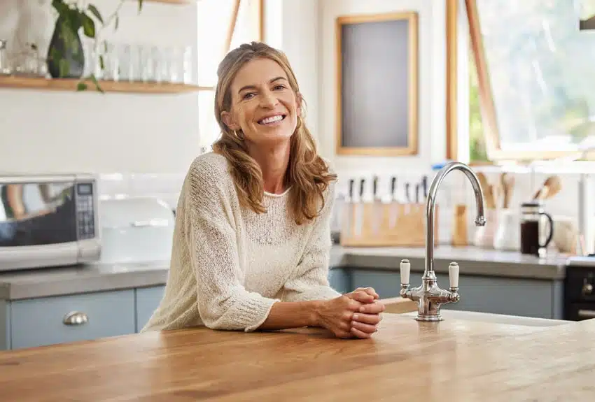mature adult woman leaning on the kitchen counter and smiling with teeth